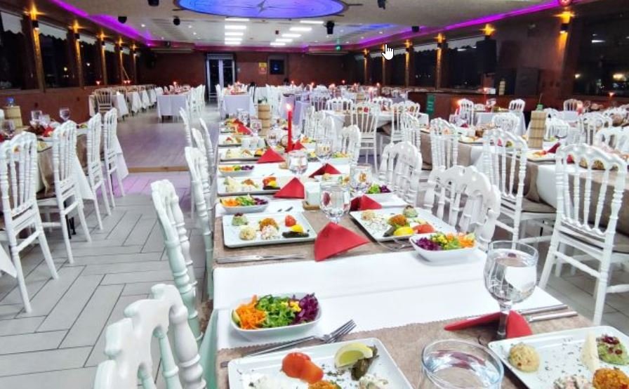 Велика зала на борту теплохода, білі накриті столи, турецькі страви, червоні серветки та фіолетова підсвітка стелі, святкова атмосфера.