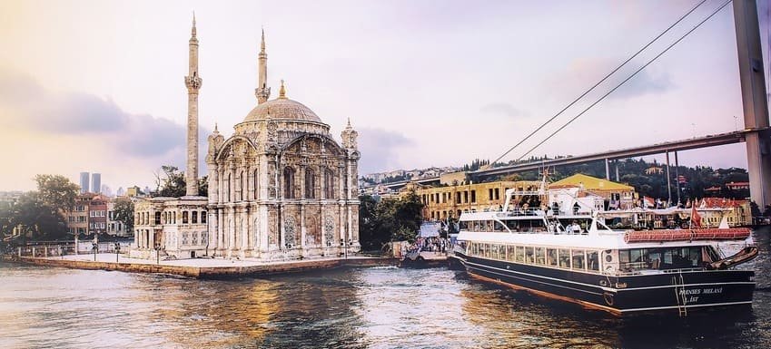 Мечеть Ортакьой на березі Босфору у Стамбулі, сучасний пором, підвісний міст над ними, м’яке вечірнє світло та спокійна атмосфера.