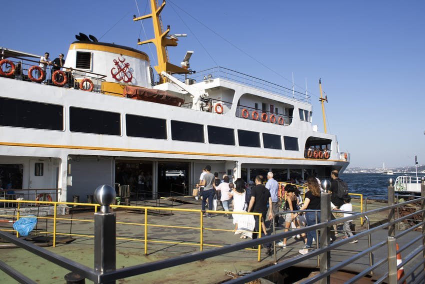 Пасажири заходять на великий білий пором біля причалу, синє море й чисте небо створюють відчуття подорожі.